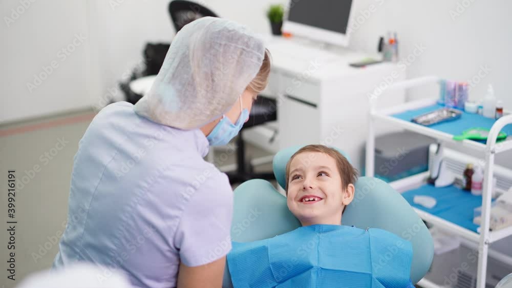 Woman Doctor in a Dental Clinic Talking with Funny Little Boy who Smiles. Work of a Dentist with Children. Healthcare and Medicine Concept. High quality 4k footage Woman Doctor in a Dental Clinic Talking with Funny Little Boy who Smiles. Work of a Dentist with Children. Healthcare and Medicine Concept. High quality 4k footage