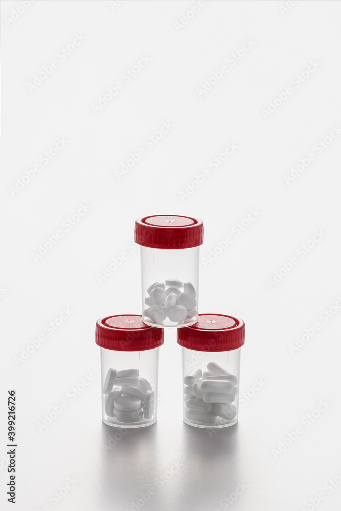 Transparent pill bottles with some pills inside and red caps forming a pyramid on white background Transparent pill bottles with some pills inside and red caps forming a pyramid on white background