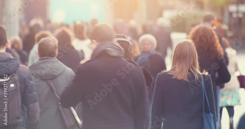 Blurred people commuting in central business district at rush hour with morning sun light. Walking commuters going to work in downtown's crowded streets, 4k video footage