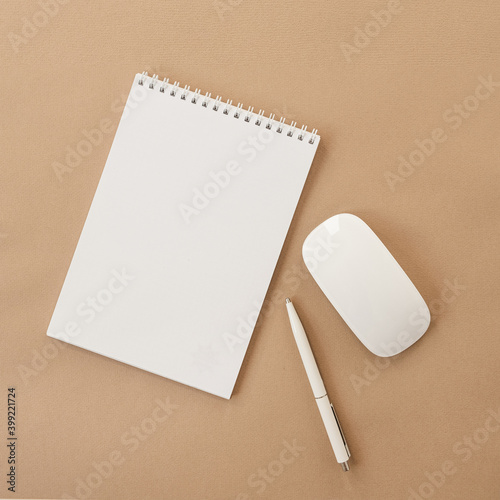 Flatlay of blank sheet spiral notebook, mouse, pen on pastel beige table. Flat lay, top view. Copy space mockup template background.