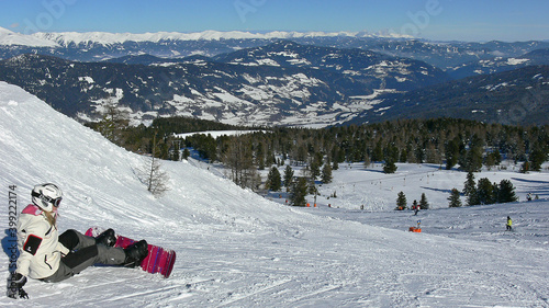 Young lady with snowboard sitting in the snow looking down to Murau Kreischberg ski area in Austria photo