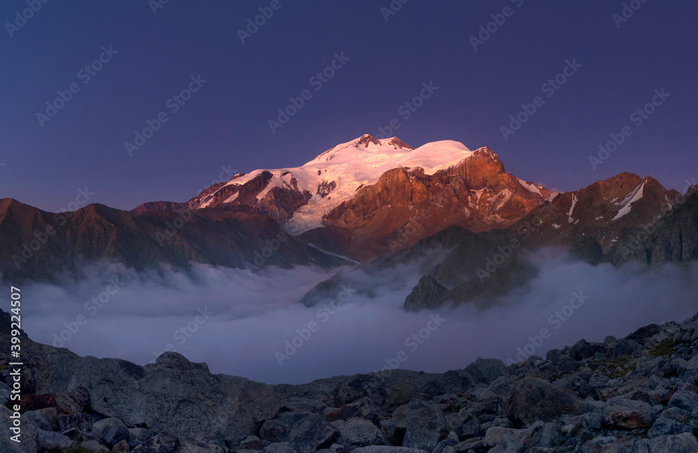 Mountain landscape. Elbrus at sunset. Clouds under the mountain. August