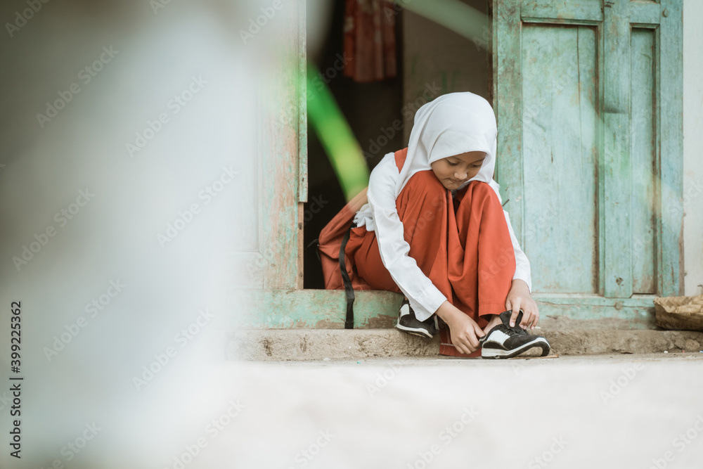 indonesian primary school student getting ready to school in the morning tying shoes in front of the house