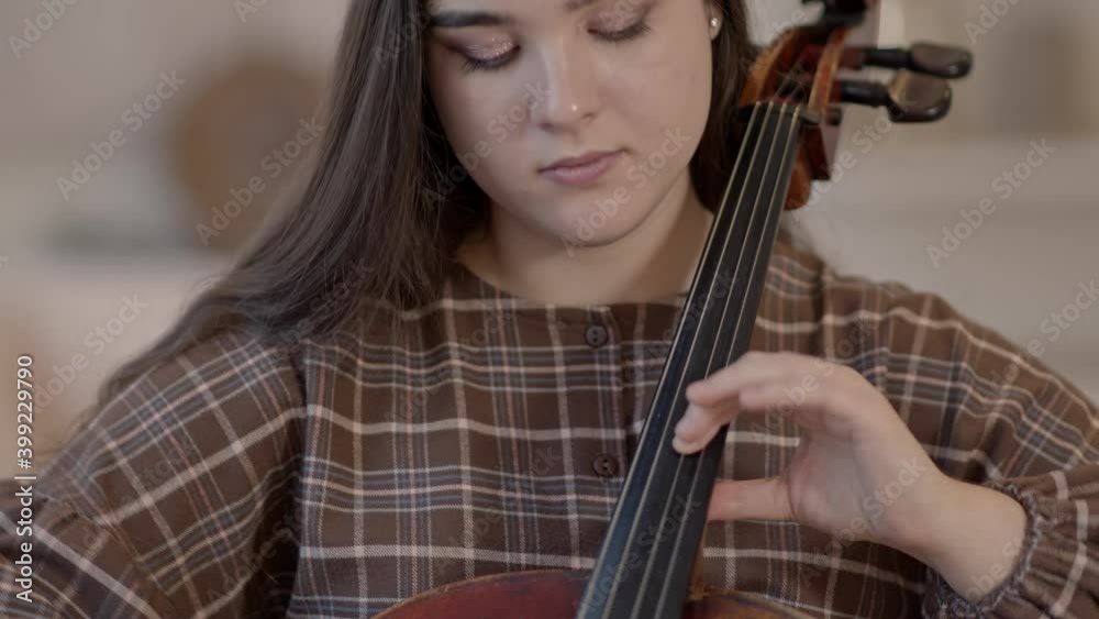 Closeup of young woman playing cello sitting on the chair at home interior. Caucasian beautiful musician woman with classical music instrument, gimbal shot Closeup of young woman playing cello sitting on the chair at home interior. Caucasian beautiful musician woman with classical music instrument, gimbal shot