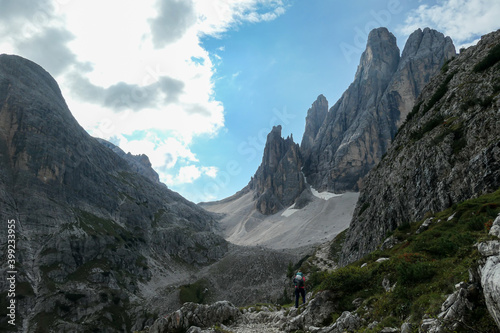 A panoramic view on Italian Dolomites. There are many high and sharp peak in front  with many landslides. Dangerous climbing. There are few trees and bushes on the side. Raw and unspoiled landscape