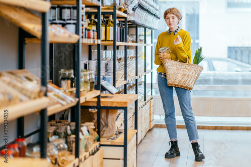 Foto Minimalist vegan style girl with wicker bag and reusable glass coffee cup on background of interior of zero waste shop