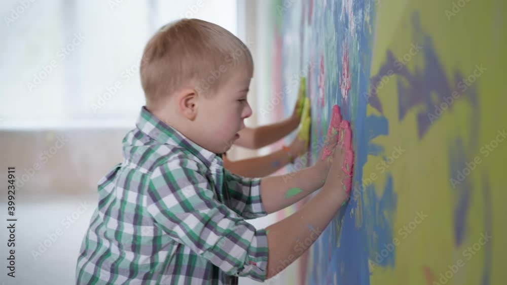 art kids paint in new home, boy with down syndrome and girl with paint on palms puts a hands on a colored wall during renovation art kids paint in new home, boy with down syndrome and girl with paint on palms puts a hands on a colored wall during renovation