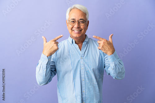 Middle age Brazilian man isolated on purple background giving a thumbs up gesture