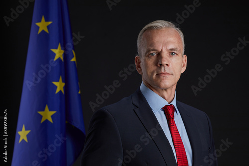 Professional portrait of handsome mature man looking at camera while standing against EU flag in background, copy space photo