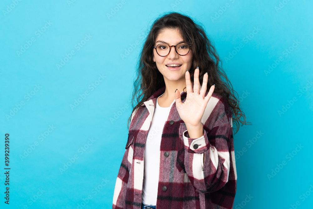 Teenager Russian girl isolated on blue background saluting with hand with happy expression Teenager Russian girl isolated on blue background saluting with hand with happy expression