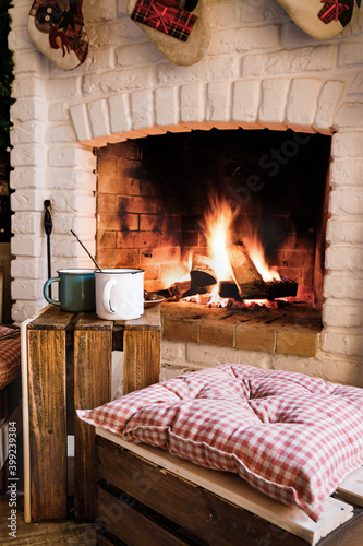 Two mugs on a wooden box against the background of a burning fireplace. Festive mood.