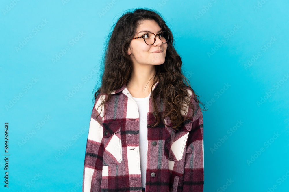 Fototapeta premium Teenager Russian girl isolated on blue background having doubts while looking up