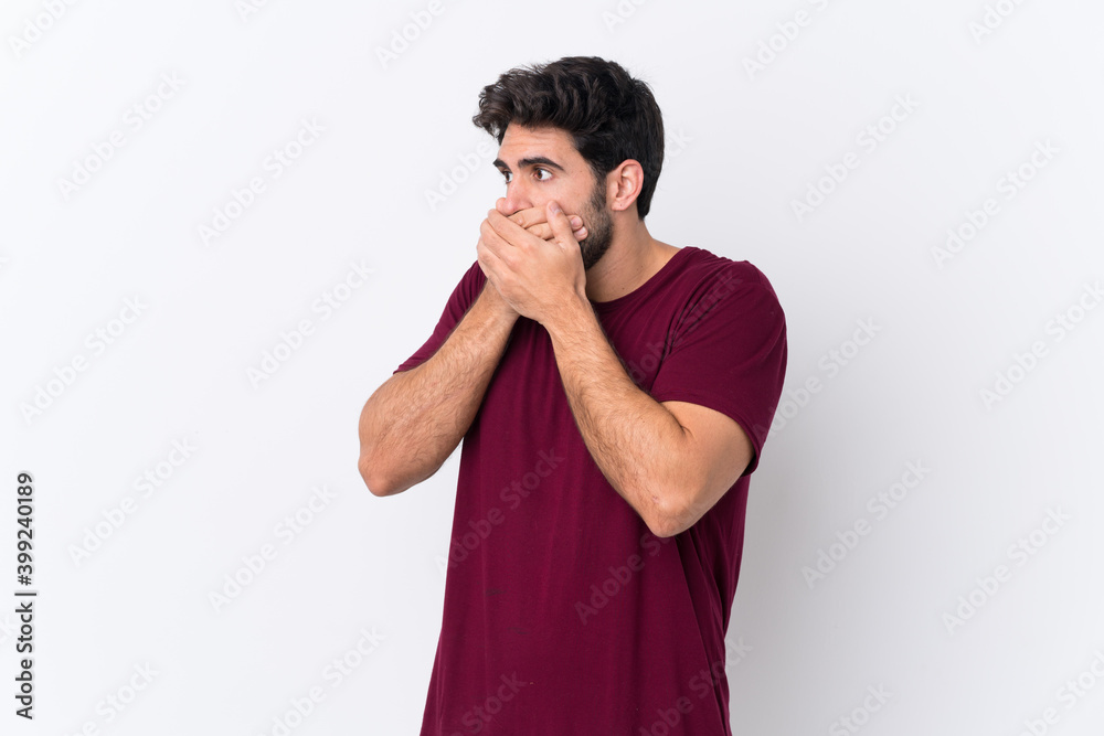Young handsome man with beard over isolated white background covering mouth and looking to the side Young handsome man with beard over isolated white background covering mouth and looking to the side