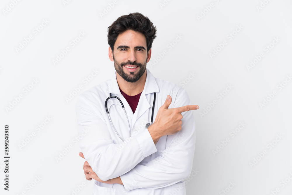 Young handsome man with beard over isolated white background wearing a doctor gown and pointing side Young handsome man with beard over isolated white background wearing a doctor gown and pointing side