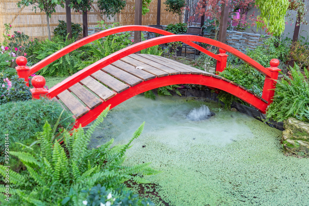 Small red wooden bridge and a pond. Garden or backyard decorating idea Small red wooden bridge and a pond. Garden or backyard decorating idea