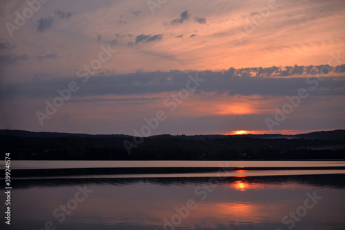 Hot sunset above the forest. Refelctions of red clouds in the water of the lake. bright colors at the end of a summer day