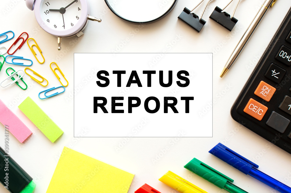 Office desk table with calculator, pens and other stationery. Text on the STATUS REPORT card. Office desk table with calculator, pens and other stationery. Text on the STATUS REPORT card.