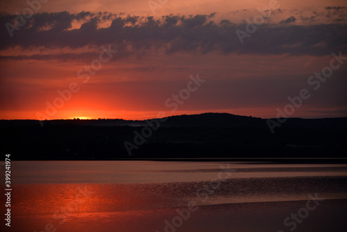 Hot sunset above the forest. Refelctions of red clouds in the water of the lake. bright colors at the end of a summer day