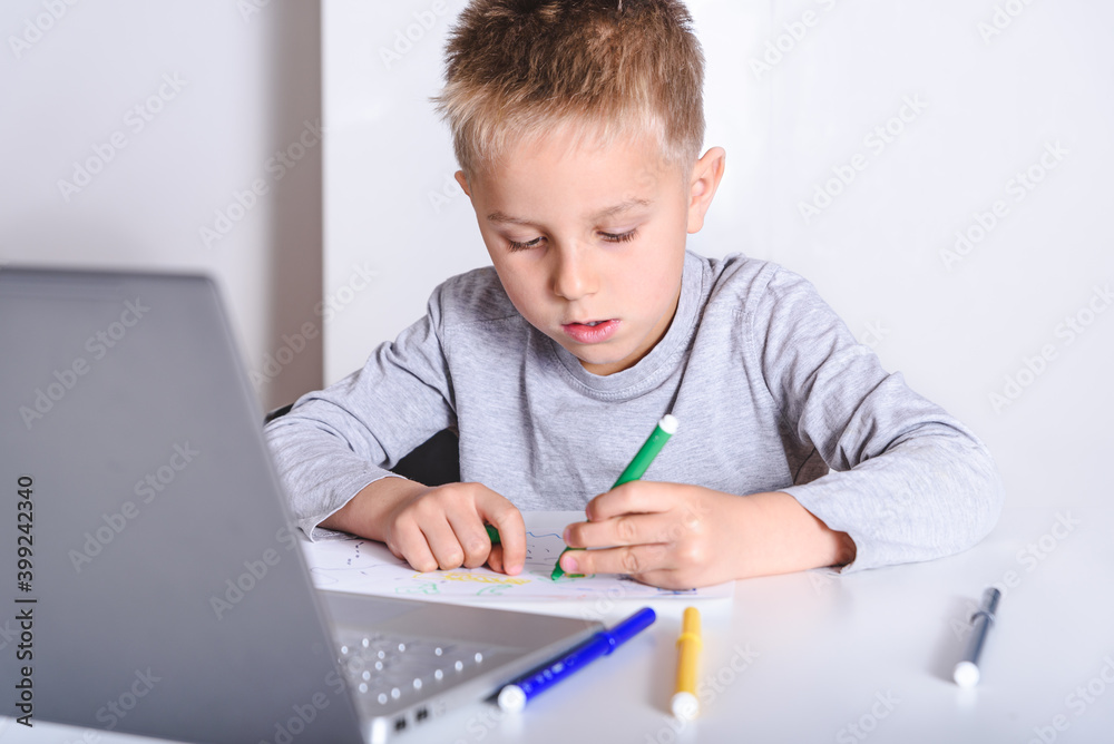 small kid drawing on a white table with a laptop near. Concept of home schooling during pandemic small kid drawing on a white table with a laptop near. Concept of home schooling during pandemic