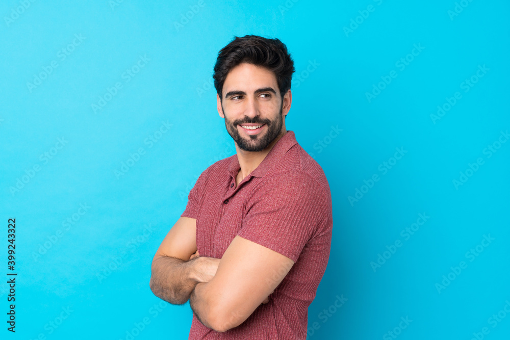 Young handsome man with beard over isolated blue background with arms crossed and happy Young handsome man with beard over isolated blue background with arms crossed and happy