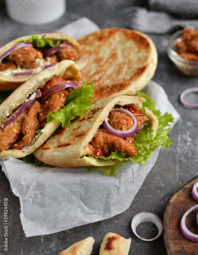 Lavash salad with fried chicken and vegetables. Pita with chicken nuggets, tomatoes, red onions and lettuce and sauce. Healthy fast food. Dark background. Vertical view