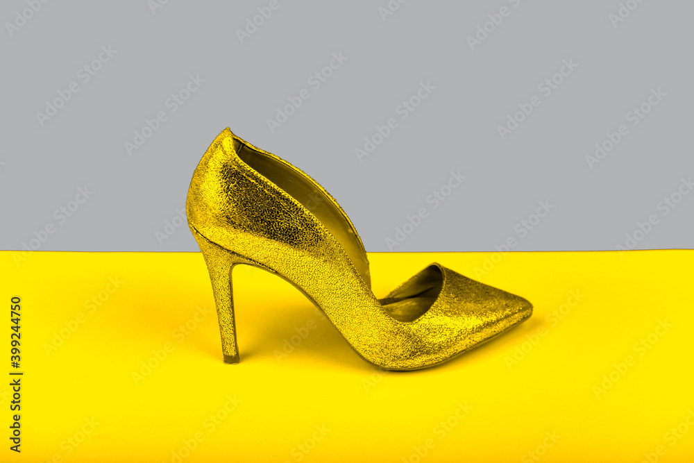 Stylish women's gold glitter shoe with medium high heels, side shot on  yellow gray multi-colored paper background. Women's fashion and style.  Stock Photo | Adobe Stock