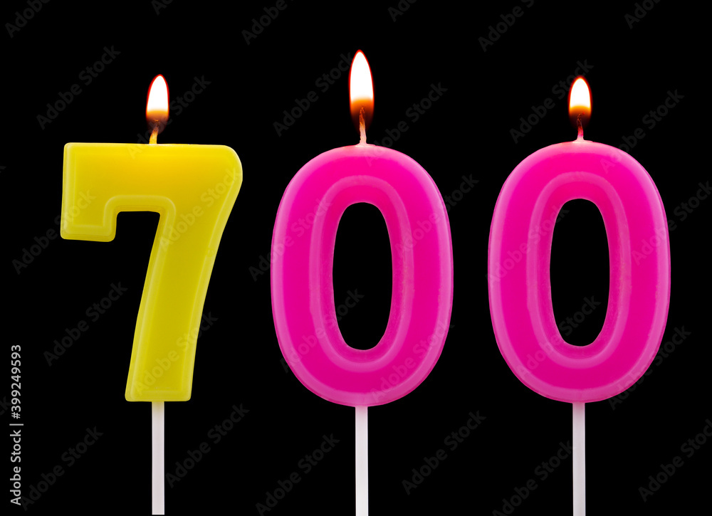 Burning birthday candles isolated on black background, number 700