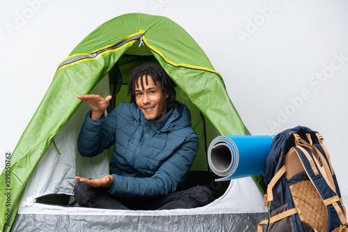 Young african american man inside a camping green tent holding copyspace to insert an ad