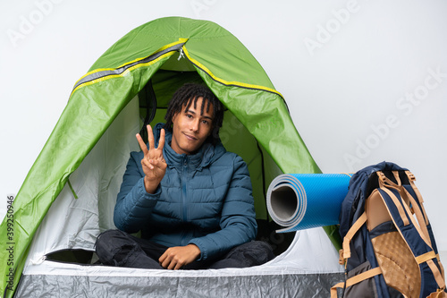 Young african american man inside a camping green tent happy and counting three with fingers
