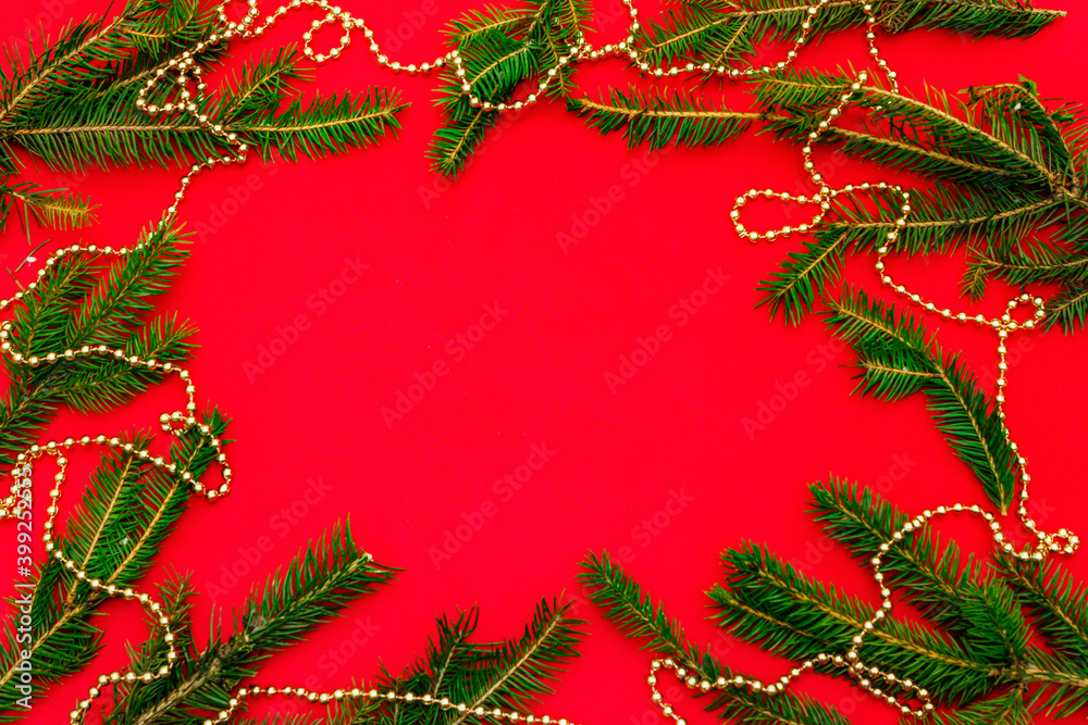 Christmas background with fresh Xmas tree branches and New Year gold beads on red background Christmas background with fresh Xmas tree branches and New Year gold beads on red background