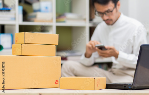 Boxes on table and laptop with man working with smartphone background , Small business, home office, package delivery, online marketing, SME e-commerce concept