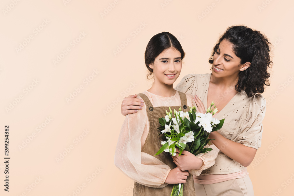 Hispanic woman hugging child with bouquet isolated on beige, two generations of women Hispanic woman hugging child with bouquet isolated on beige, two generations of women