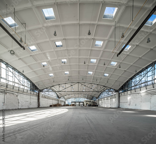 Stack wooden pallets in huge empty industrial warehouse. White interior. Hemispherical reinforced concrete load bearing roof with windows. Modern architecture.