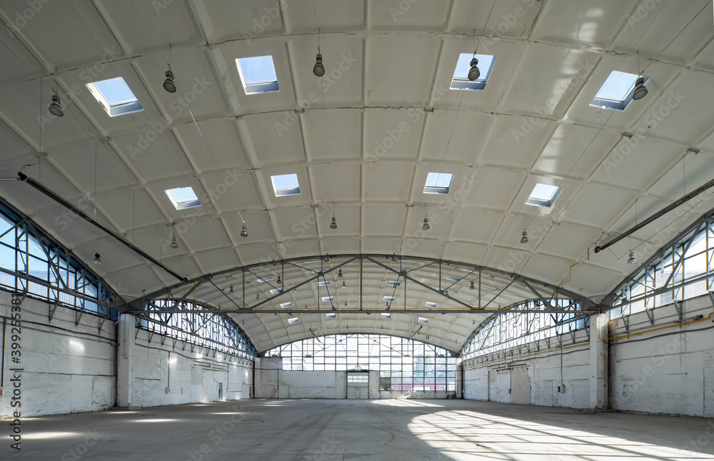 Huge empty industrial warehouse. White interior. Unique architecture. Hemispherical reinforced concrete load bearing roof with windows. Modern building.