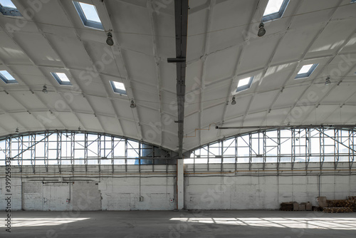 Huge empty industrial warehouse. White interior. Unique architecture. Hemispherical reinforced concrete load bearing roof with windows. Wooden pallets near wall.