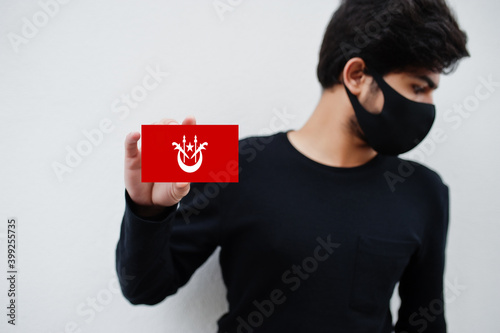 Malay man wear all black with face mask hold Kelantan flag in hand isolated on white background. States and federal territories of Malaysia coronavirus country concept. photo