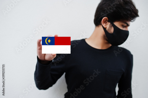 Malay man wear all black with face mask hold Malacca flag in hand isolated on white background. States and federal territories of Malaysia coronavirus country concept. photo