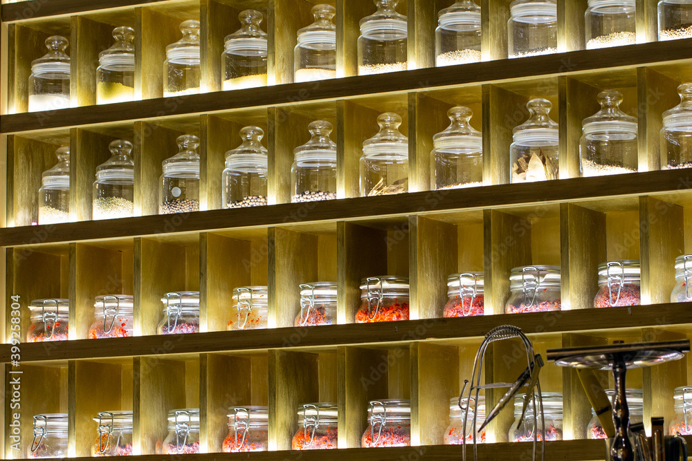 Tea and various spices in glass jars on shelves with lighting. Sale of tea in the store