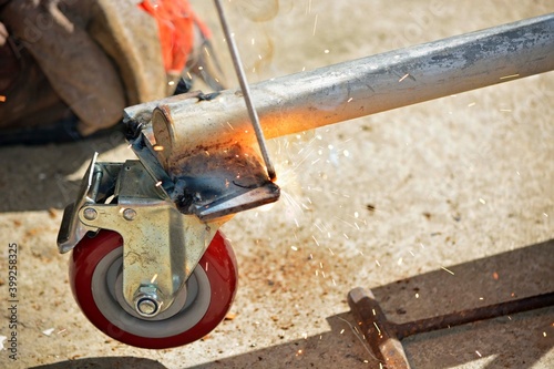 Worker with a welding machine fixing a caster wheels, sparks flying around