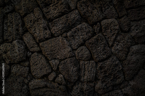 coarse-textured black background with many holes in basalt stone. © J. studio