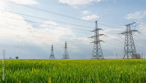 High voltage lines and power pylons and a green agricultural landscape on a sunny day.
