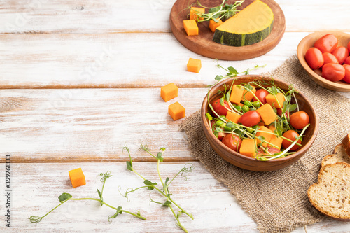 Vegetarian vegetable salad of tomatoes, pumpkin, microgreen pea sprouts on white wooden background. Side view, copy space.
