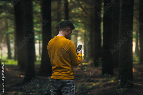 person with yellow jacket and gray jeans looking at the phone in the forest