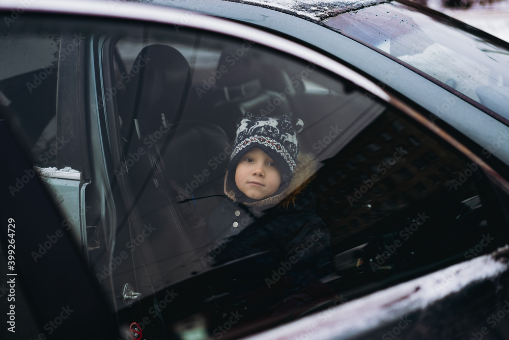 6 year old caucasian boy sitting in a car on passenger seat. View through the door window. Image with selective focus