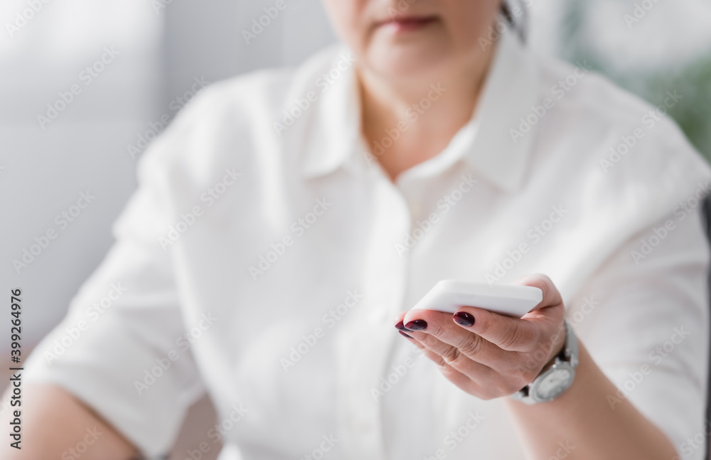 Cropped view of plus size hispanic businesswoman holding smartphone on blurred background Cropped view of plus size hispanic businesswoman holding smartphone on blurred background