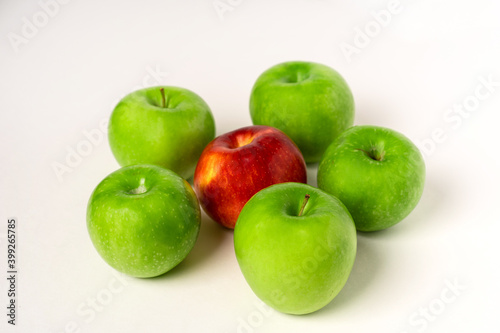 Green apples and one red one are laid out on a white table