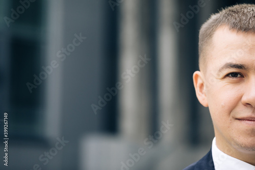 Close up of half face of upset Caucasian young businessman in looking straight to camera while standing outdoors near modern office building