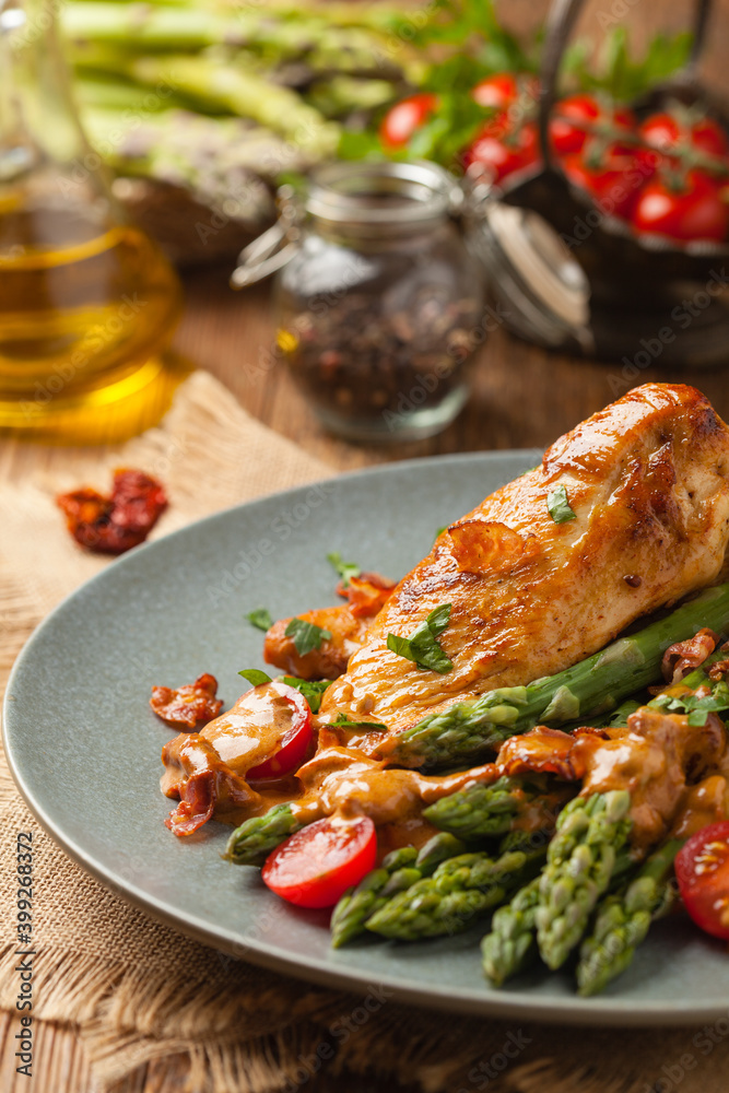 Roasted chicken breast, served on asparagus with tomato sauce, dried tomatoes. Front view.