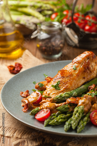 Roasted chicken breast, served on asparagus with tomato sauce, dried tomatoes. Front view.