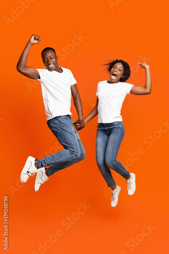 Emotional black couple holding hands and jumping up
